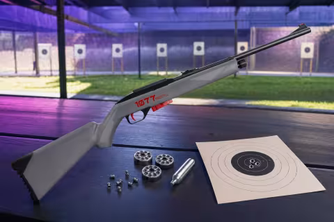 Crosman 1077 FreeStyle s rotačnými klipmi, CO₂ bombičkou a terčom na streleckom stole.