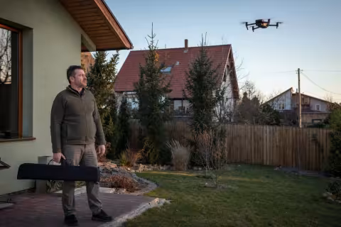 Cudzí kamerový dron nad záhradou rodinného domu a majiteľ so zatvoreným puzdrom na zbraň.