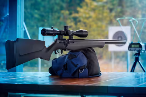 FX Airguns DRS Classic s orechovou pažbou a vzduchovým zásobníkom okolo hlavne na streleckom stole.